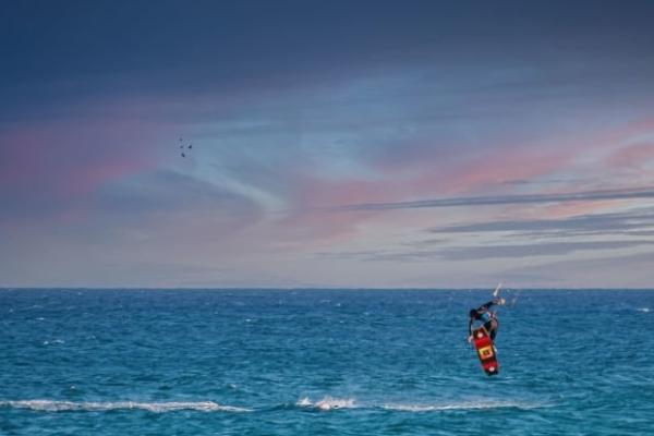 Kitesurfista salta sopra l'oceano al tramonto, cielo colorato di rosa e blu.