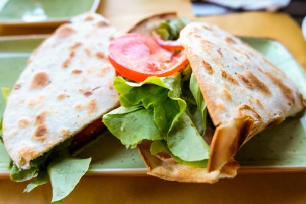 Piadina ripiena di lattuga e pomodoro su piatto verde.