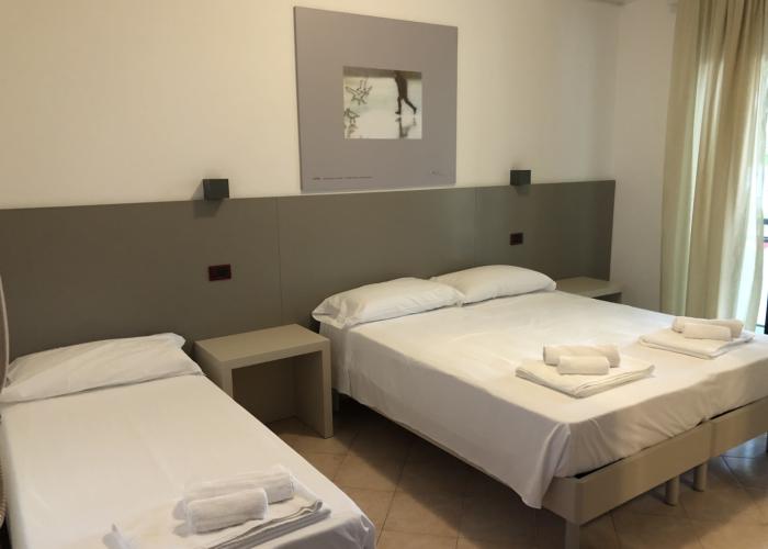 Camera d'albergo moderna con tre letti e asciugamani piegati.