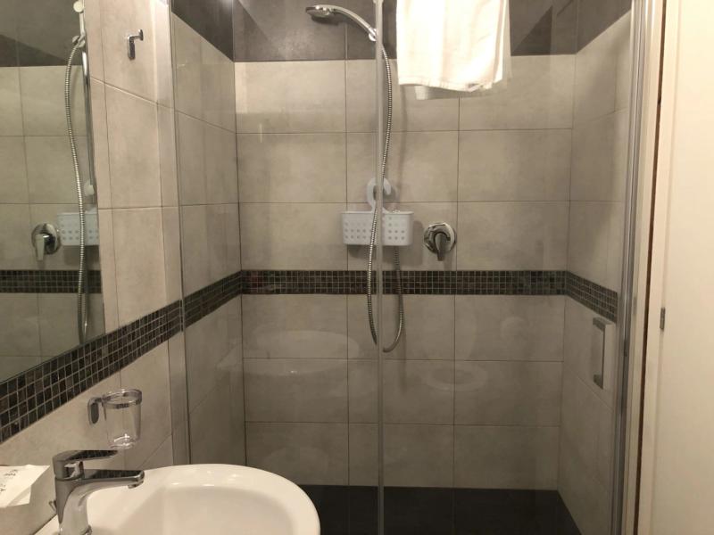 Bagno moderno con doccia a piastrelle, lavabo e accessori cromati.