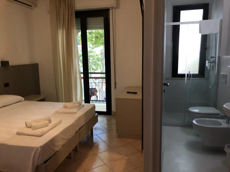 Camera d'albergo moderna con bagno privato e balcone, letti ordinati e asciugamani.