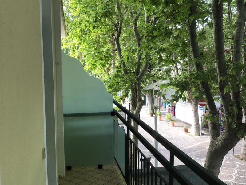 Balcone con ringhiera nera, pavimento piastrellato e vista su alberi verdi.
