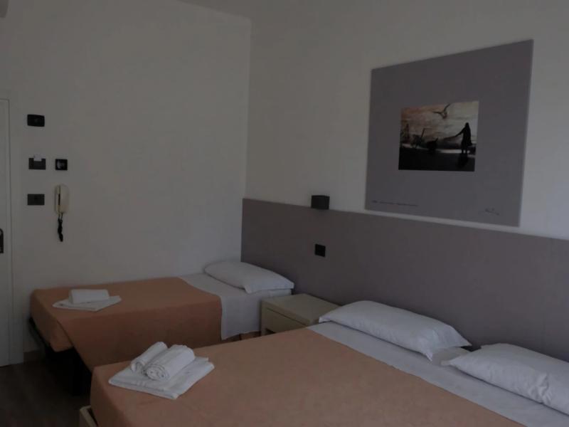 Camera d'albergo con due letti singoli e asciugamani piegati, decorata con un quadro.