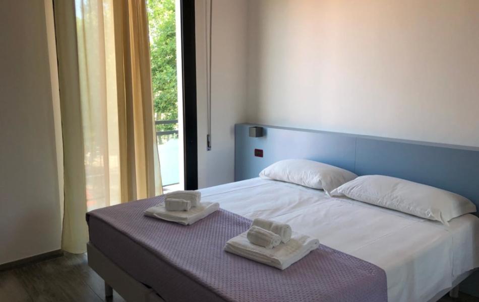 Camera da letto moderna con letto matrimoniale e asciugamani piegati, vista su balcone.