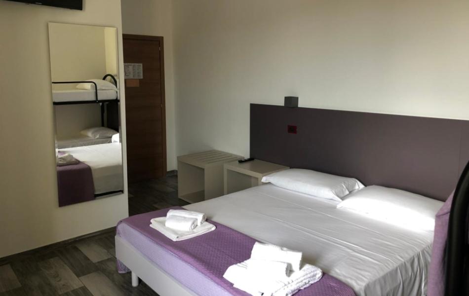 Camera d'albergo con letto matrimoniale, letti a castello, TV e aria condizionata.