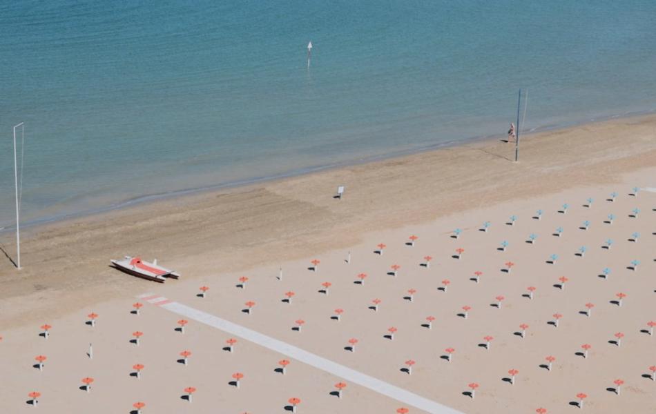 Spiaggia deserta con file di ombrelloni chiusi e un pattino rosso sulla sabbia.